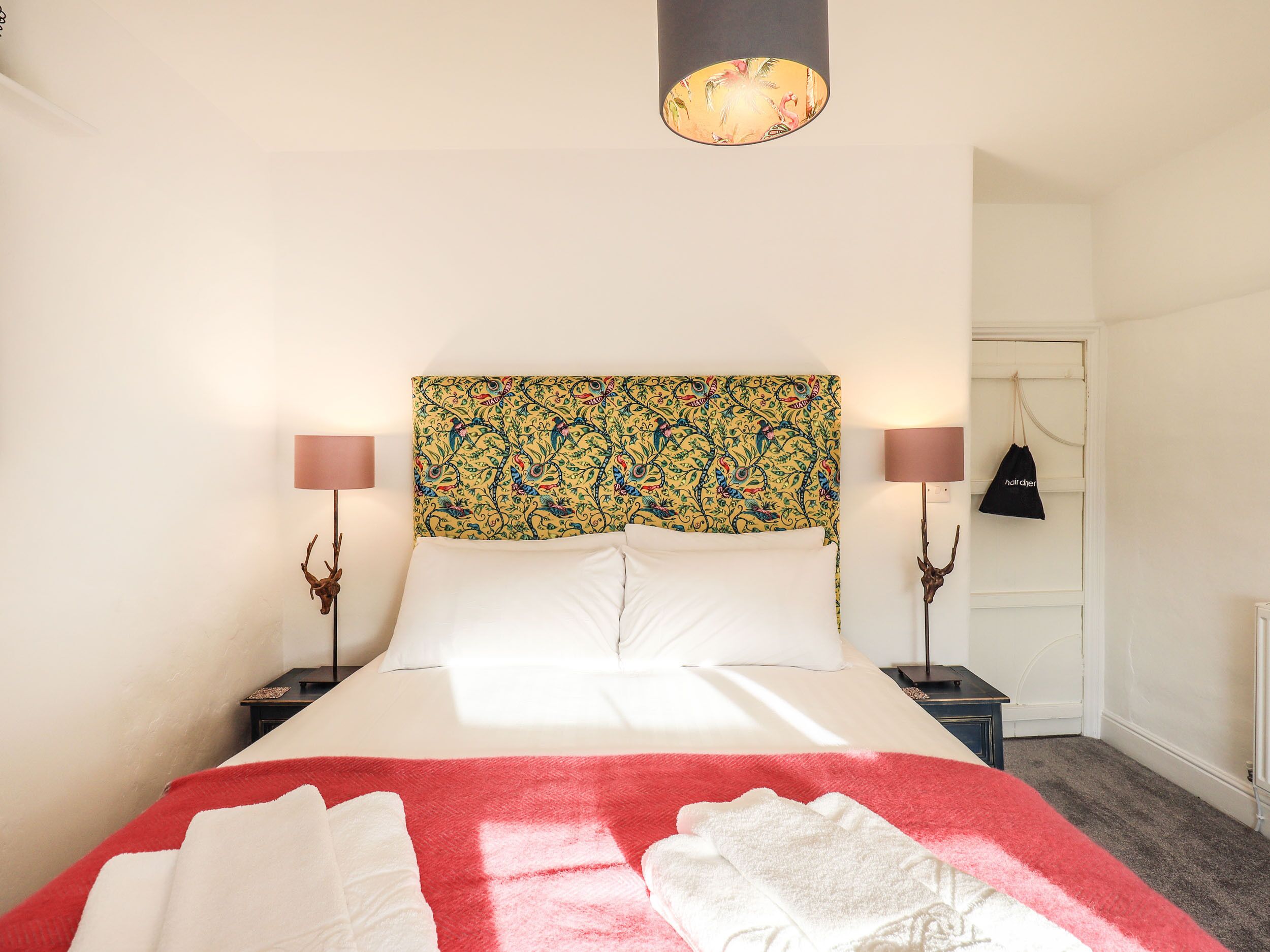 A neatly made bed with white linens, a colorful headboard, and two bedside lamps.