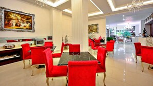 Un coin repas avec des chaises à revêtement rouge, une table en marbre noir et un grand tableau accroché au mur.