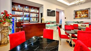 Un restaurant avec des chaises rouges, une table en marbre noir, un bar où sont exposées différentes bouteilles, et un tableau accroché au mur.