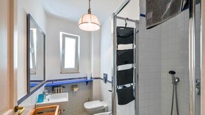 Een badkamer met een houten bankje, een wastafel, toilet, bidet en douche met glazen deur.