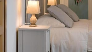 Een slaapkamer met een bed, een nachtkastje met een lamp en een schilderij aan de muur.