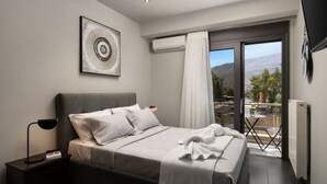 Ein Schlafzimmer mit einem Bett, einem Nachttisch mit Lampe, einem gerahmten Bild an der Wand und Blick ins Freie durch eine Schiebetür.