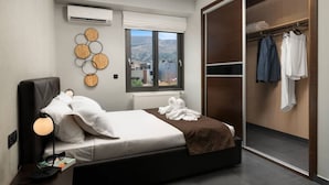 Ein modernes Schlafzimmer mit Bett, Nachttischlampe, Klimaanlage, Fenster mit Blick und einem begehbaren Kleiderschrank mit Kleidung.