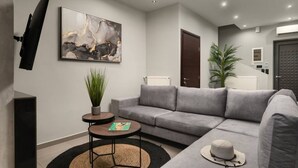 Ein modernes Wohnzimmer mit einem grauen Sofa, einem kleinen runden Tisch mit einer Pflanze und einem Bild an der Wand.