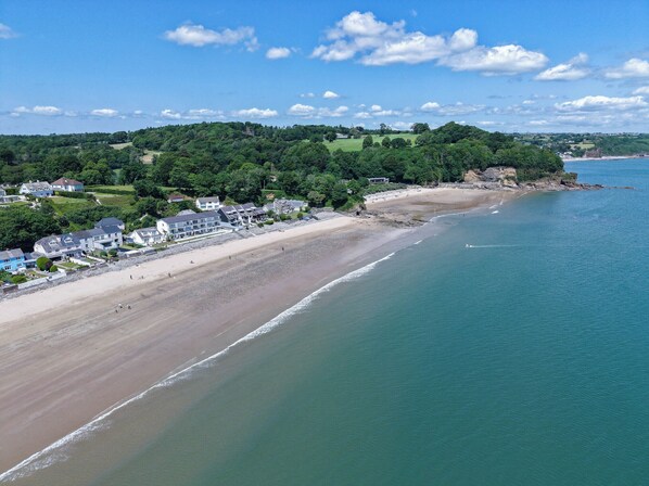 A coastal area with a beach, houses, and a forested hill.