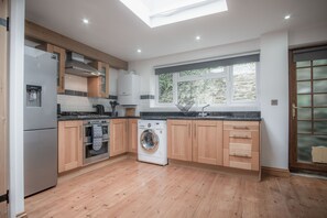 Eine moderne Küche mit Holzausstattung, einem Edelstahl-Kühlschrank, einer Waschmaschine und einem großen Fenster, das für natürliches Licht sorgt.