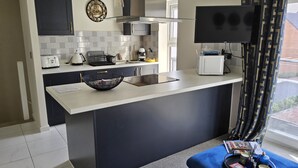 A modern kitchen with a large island, a flat-screen TV, and a decorative wall clock. - Luxury Small Cozy House With Lake View (Doncaster)