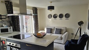 A modern kitchen with a central island, a dining area with a sofa, and a living room with a black armchair. There are clocks on the wall indicating different cities. - Luxury Small Cozy House With Lake View (Doncaster)
