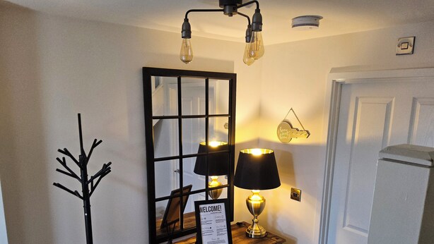 A reception area with a wooden console, a welcome sign, a mirror, and a wall-mounted key holder. - Luxury Small Cozy House With Lake View (Doncaster)