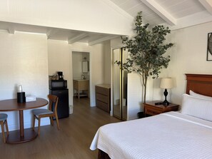 A hotel room with a bed, a desk with a chair, a small table, a plant, and a mirror. - One King bedroom Cottage (Carmel-by-the-Sea)