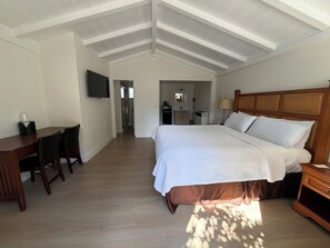 A bedroom with a large bed, a desk, and a TV on the wall.