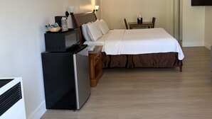 A hotel room with a bed, a desk with a computer, a refrigerator, a TV, and a window. - One King bedroom Cottage (Carmel-by-the-Sea)