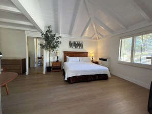 A bedroom with a bed, bedside tables, a potted plant, a mirror, and a window with blinds. - One King bedroom Cottage (Carmel-by-the-Sea)