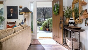 A cozy living room with a sofa, a lamp, a door leading to a garden, and various decorative items. - Château Vigne: Luxe retreat, Hot Tub, plunge pool, Outdoor movies, game room, EV (Atascadero)
