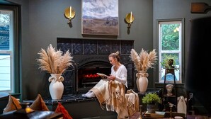 A cozy living room with a fireplace, two vases with pampas grass, and a person reading a book. - Château Vigne: Luxe retreat, Hot Tub, plunge pool, Outdoor movies, game room, EV (Atascadero)