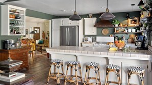 A modern kitchen with a large island, bar stools, and a dining area with a sofa and table. - Château Vigne: Luxe retreat, Hot Tub, plunge pool, Outdoor movies, game room, EV (Atascadero)