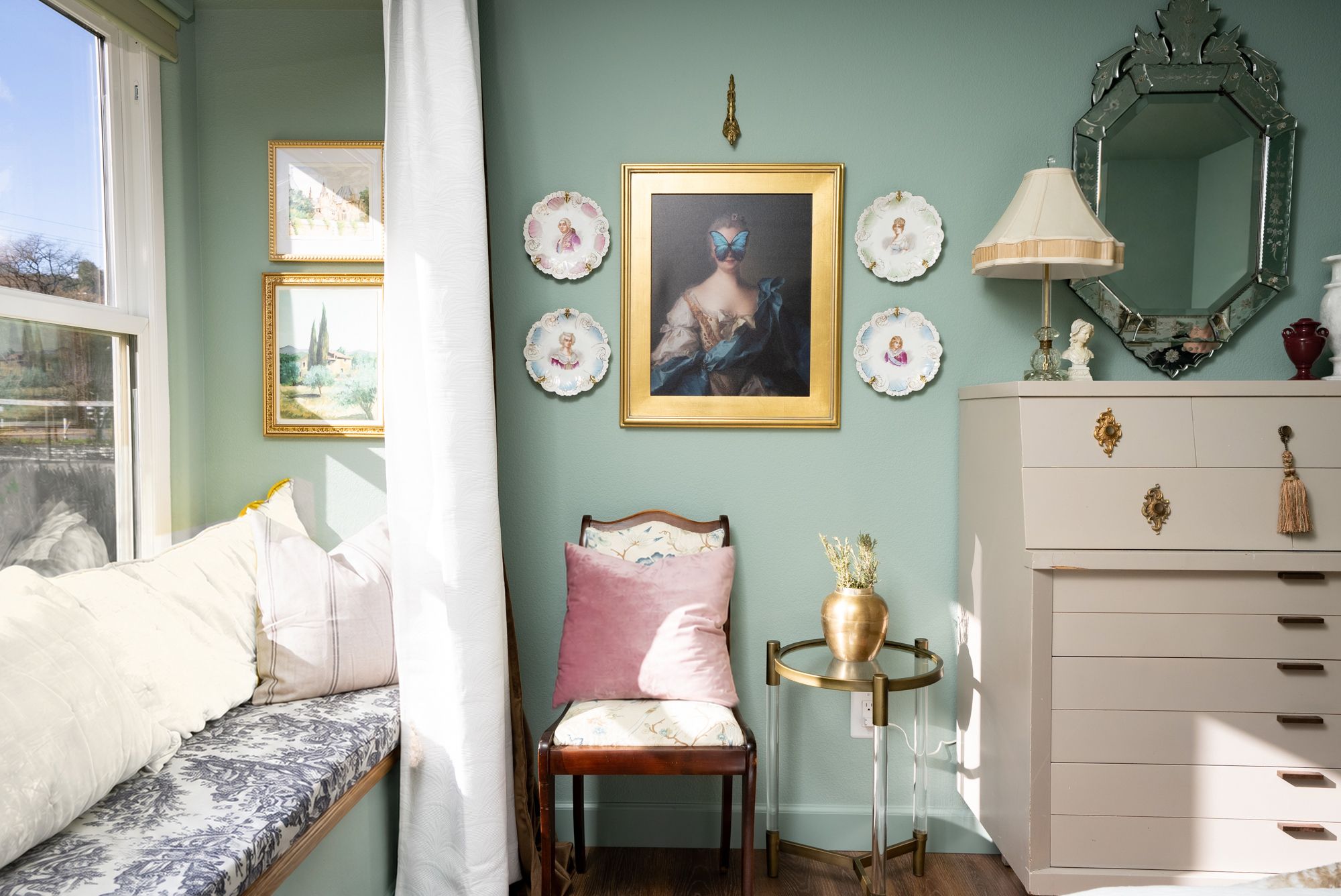 Una habitación con cama, una silla, cómoda, espejo y decoración en la pared, incluyendo cuadros y platos enmarcados.