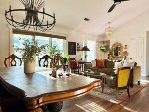 A spacious living room with a large wooden dining table, a chandelier, and a ceiling fan.