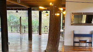 Een interieur met een houten vloer, grote pilaren en hangende lampen. Er staat een bank en er hangt een spiegel aan de muur.