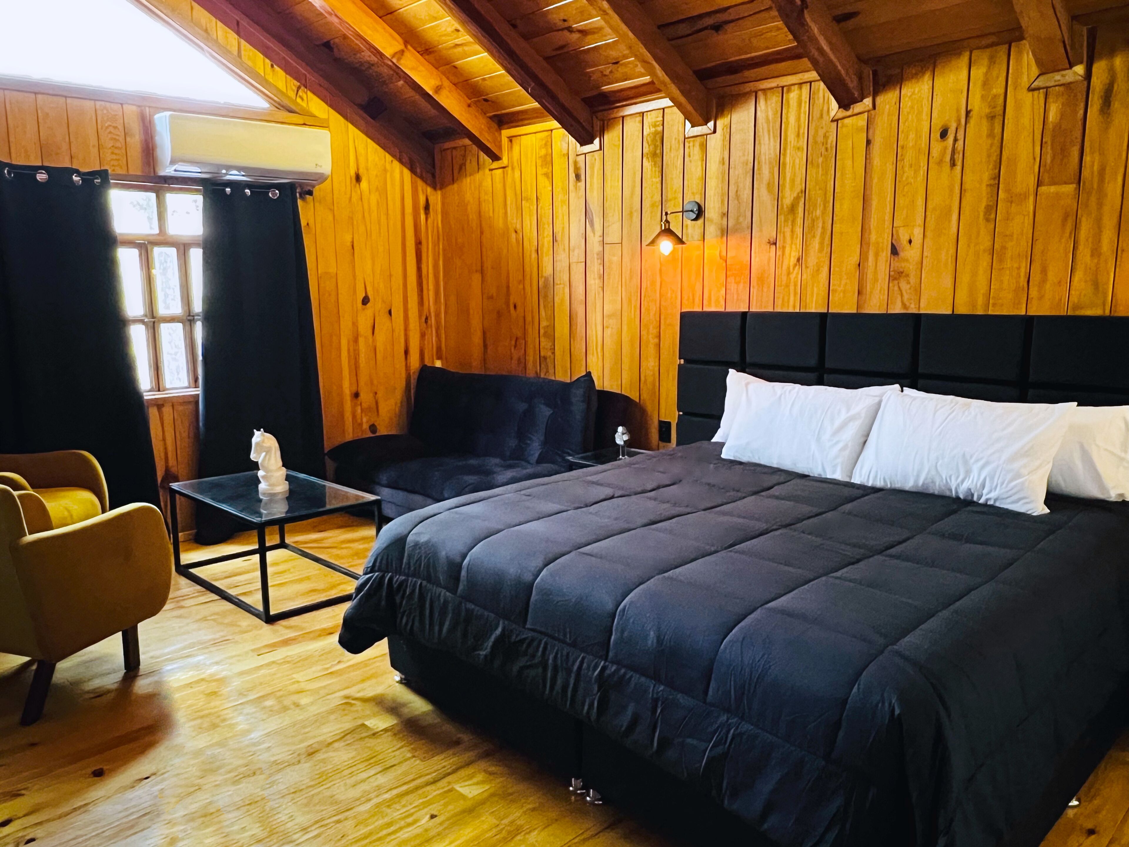 A wooden-paneled room with a bed, a small table, and a chair.