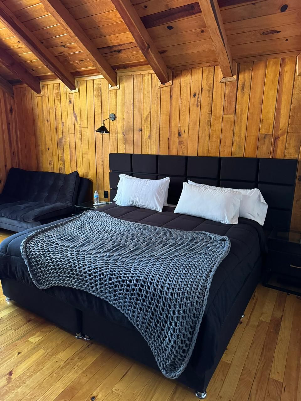 Ein Zimmer mit Holzwandverkleidung, einem Bett, einem schwarzen Kopfteil und einer schwarzen Couch.