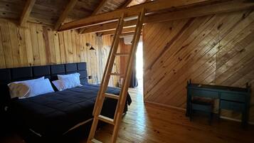 Une pièce en bois avec un plafond en pente, un lit avec des oreillers blancs, une échelle en bois et un bureau.