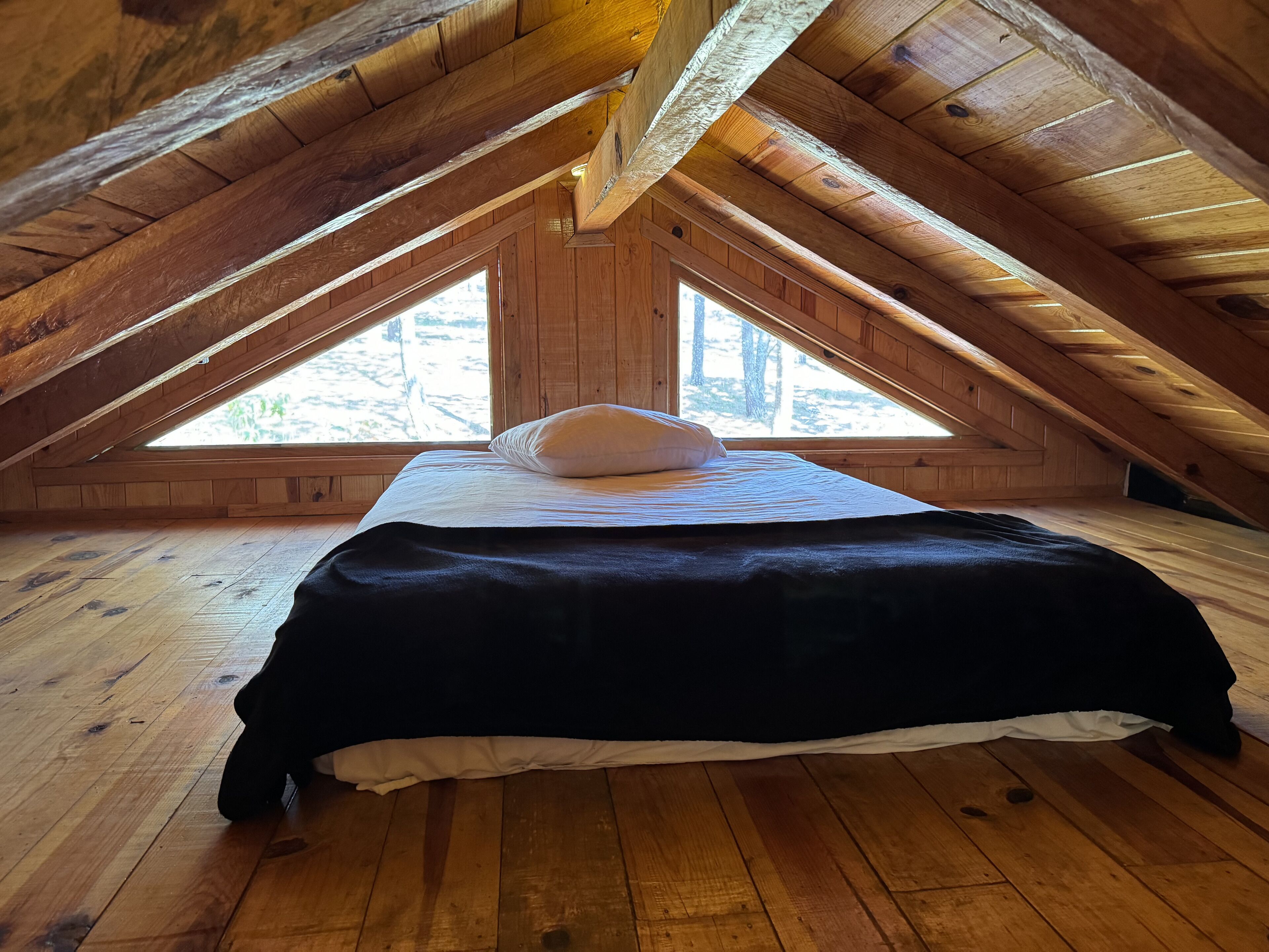 Un dormitorio con techo inclinado, paredes de madera, una cama con almohada blanca y una manta negra.