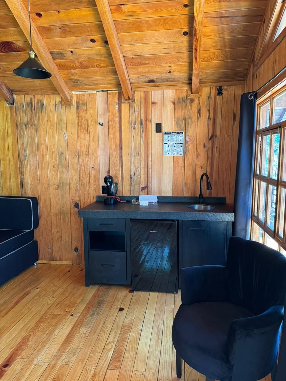 Una cocina compacta con paredes de madera, un lavamanos y un refrigerador pequeño.