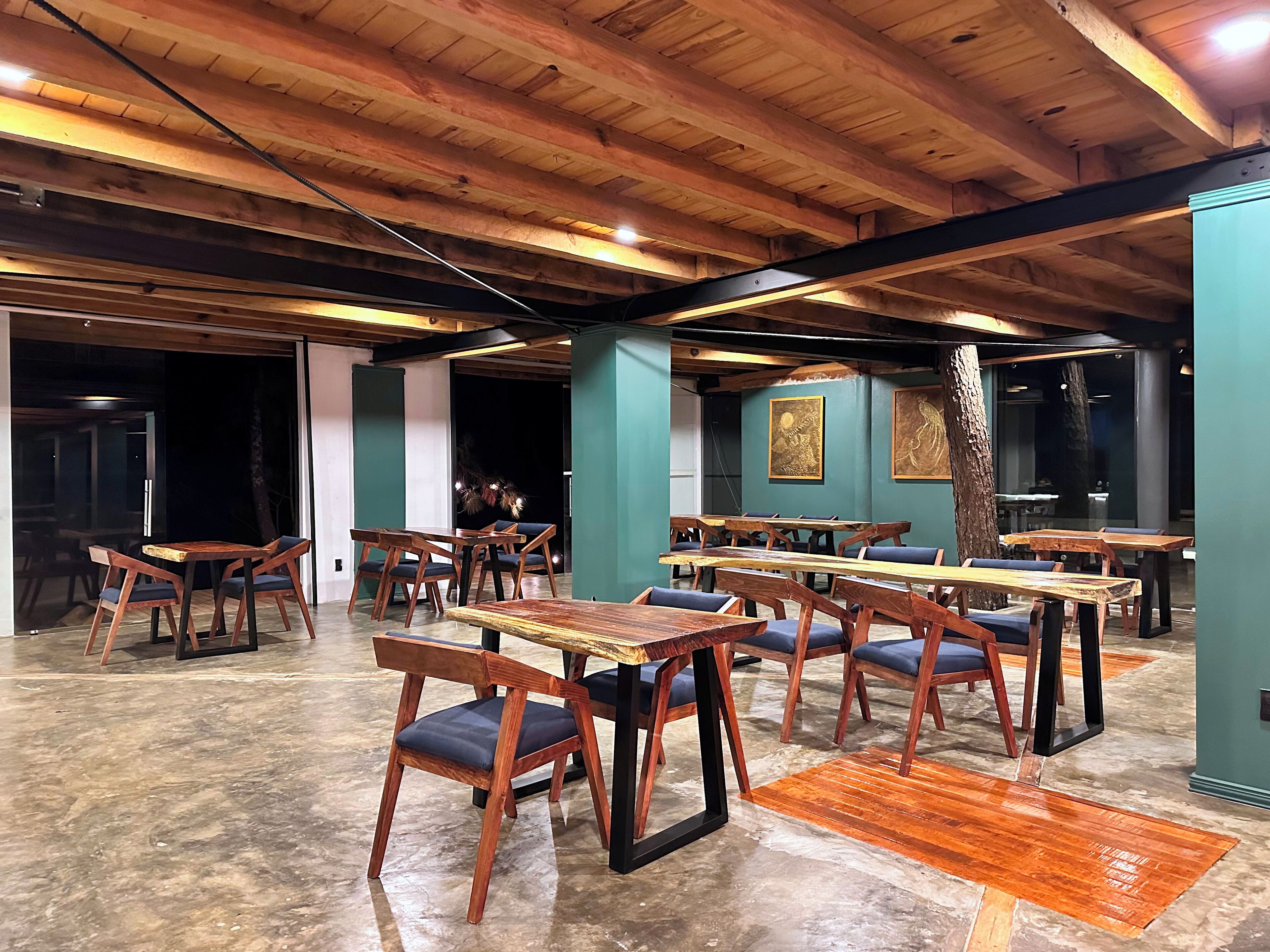 A spacious restaurant with wooden tables and chairs, a high ceiling with exposed beams, and a view of the outside through large windows.