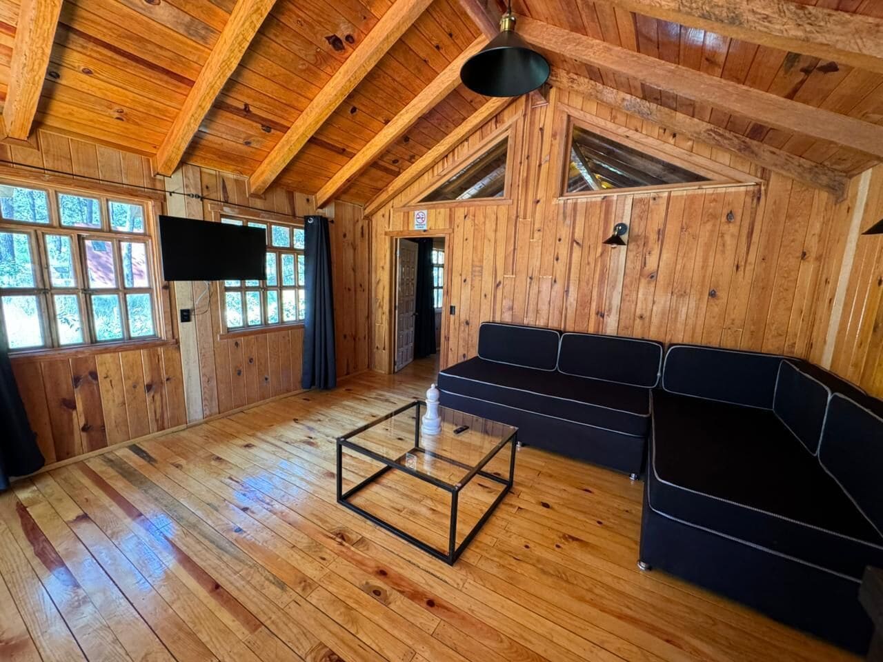 A wooden interior with a sofa, a glass coffee table, and a TV mounted on the wall.