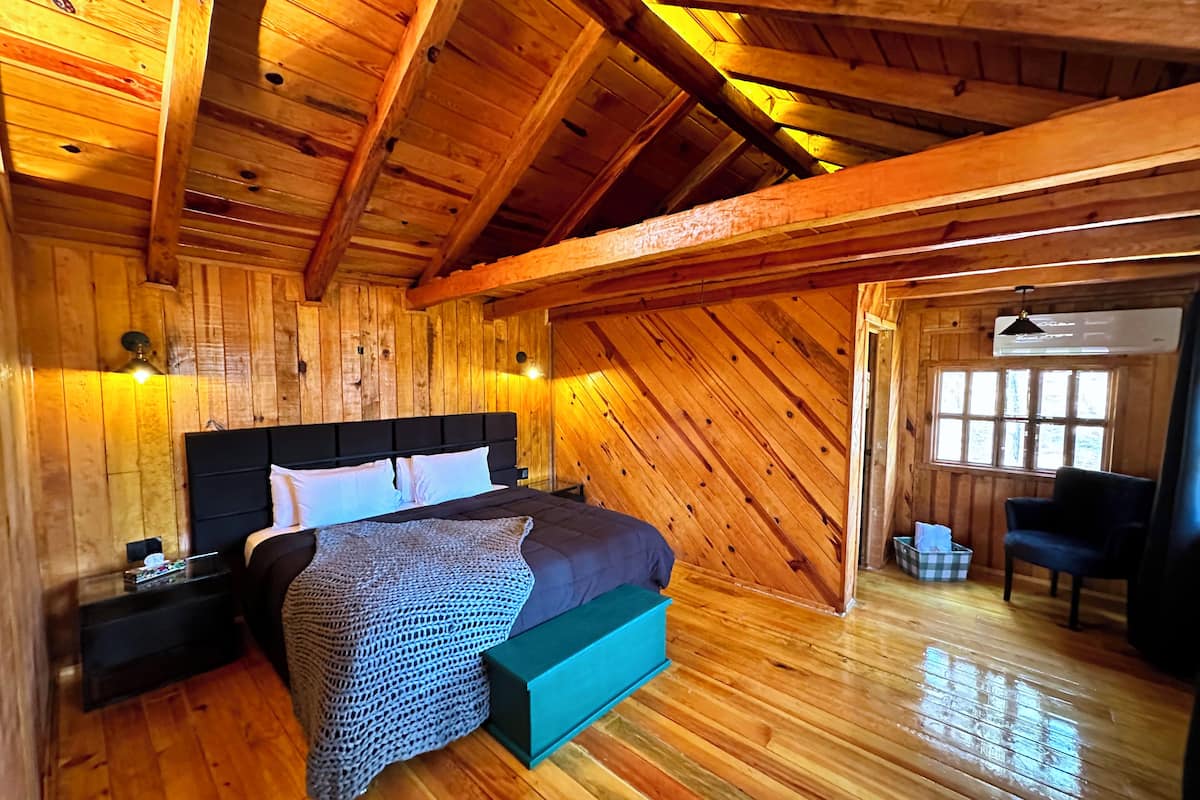 Un dormitorio de cabaña de madera con cama, mesitas de noche y ventana.