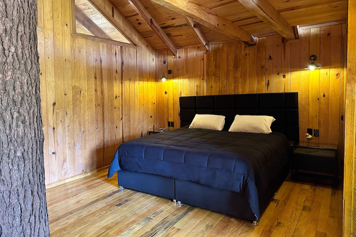 Un dormitorio de cabaña de madera con una cama grande, paredes de madera y techo inclinado.