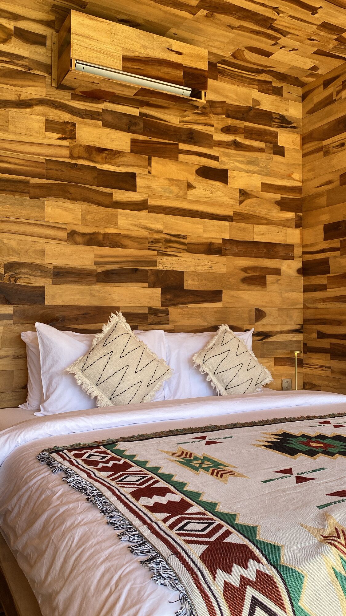 A bedroom with a wooden wall panel design, a bed with white bedding, and a patterned throw blanket.