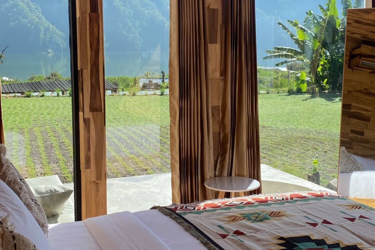 A bedroom with a large bed, wooden ceiling, and a view of a lush landscape.