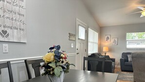 En matplats med ett bord, stolar och en vas med blommor. I bakgrunden finns en vägg med en skylt och en dörr.