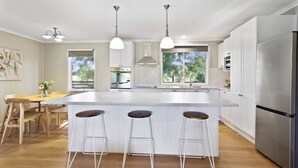 Una cocina moderna con una isla grande, taburetes de bar, electrodomésticos de acero inoxidable y un comedor con mobiliario de madera.