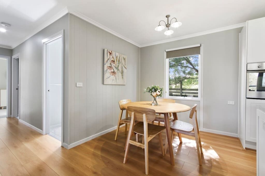 Una cocina moderna con piso de madera, una mesa de comedor con sillas, una ventana con persianas y una lámpara en el techo.