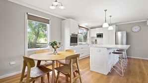 Una cocina moderna con armarios blancos, una isla central con taburetes y una zona de comedor con mesa y sillas de madera.