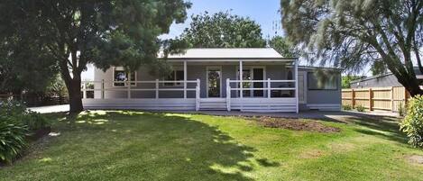 A single-story house with a porch, surrounded by a well-maintained lawn and trees.