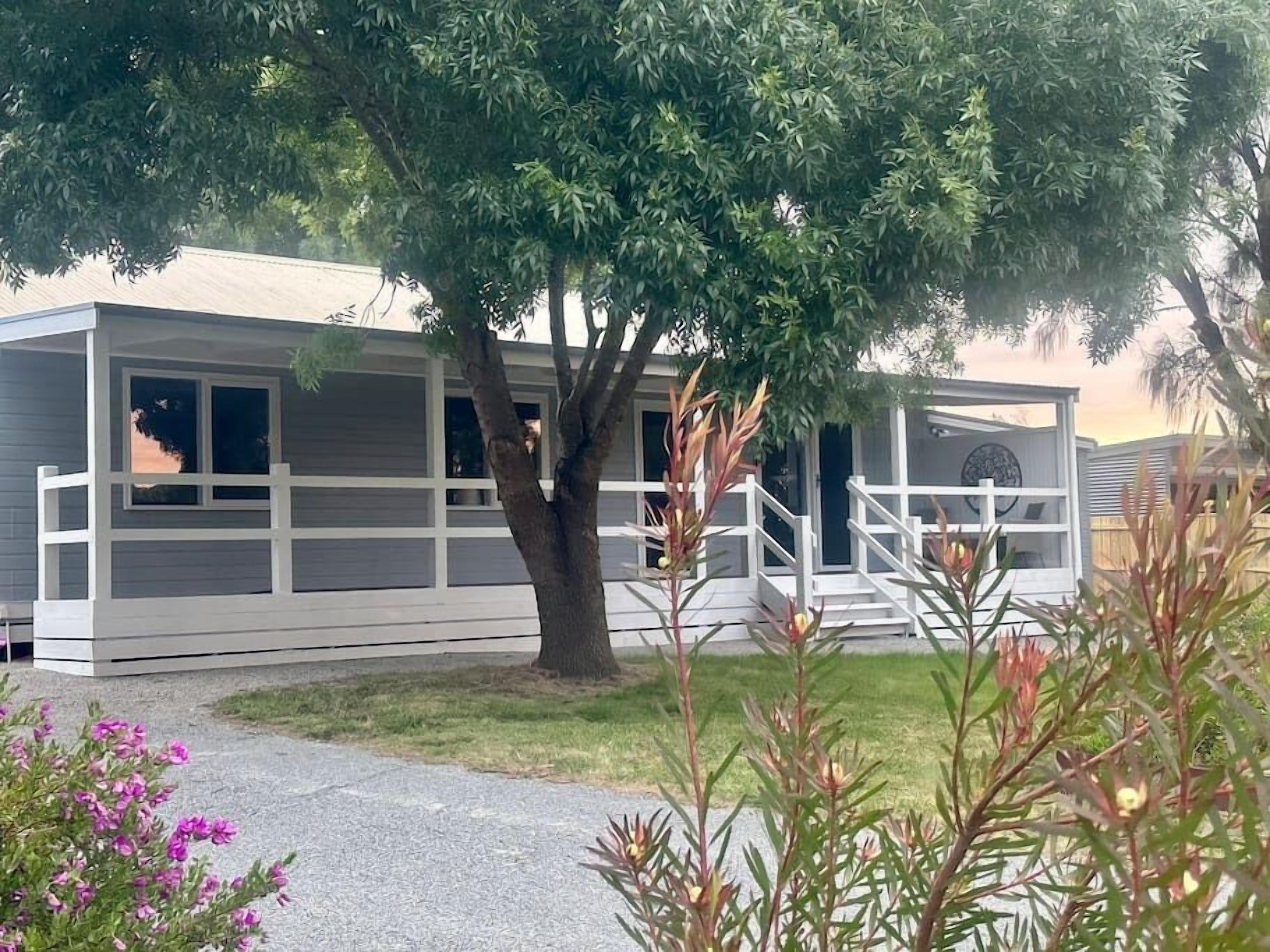 A single-story mobile home with a covered porch and a tree in front.