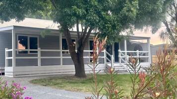 A single-story mobile home with a covered porch and a tree in front.