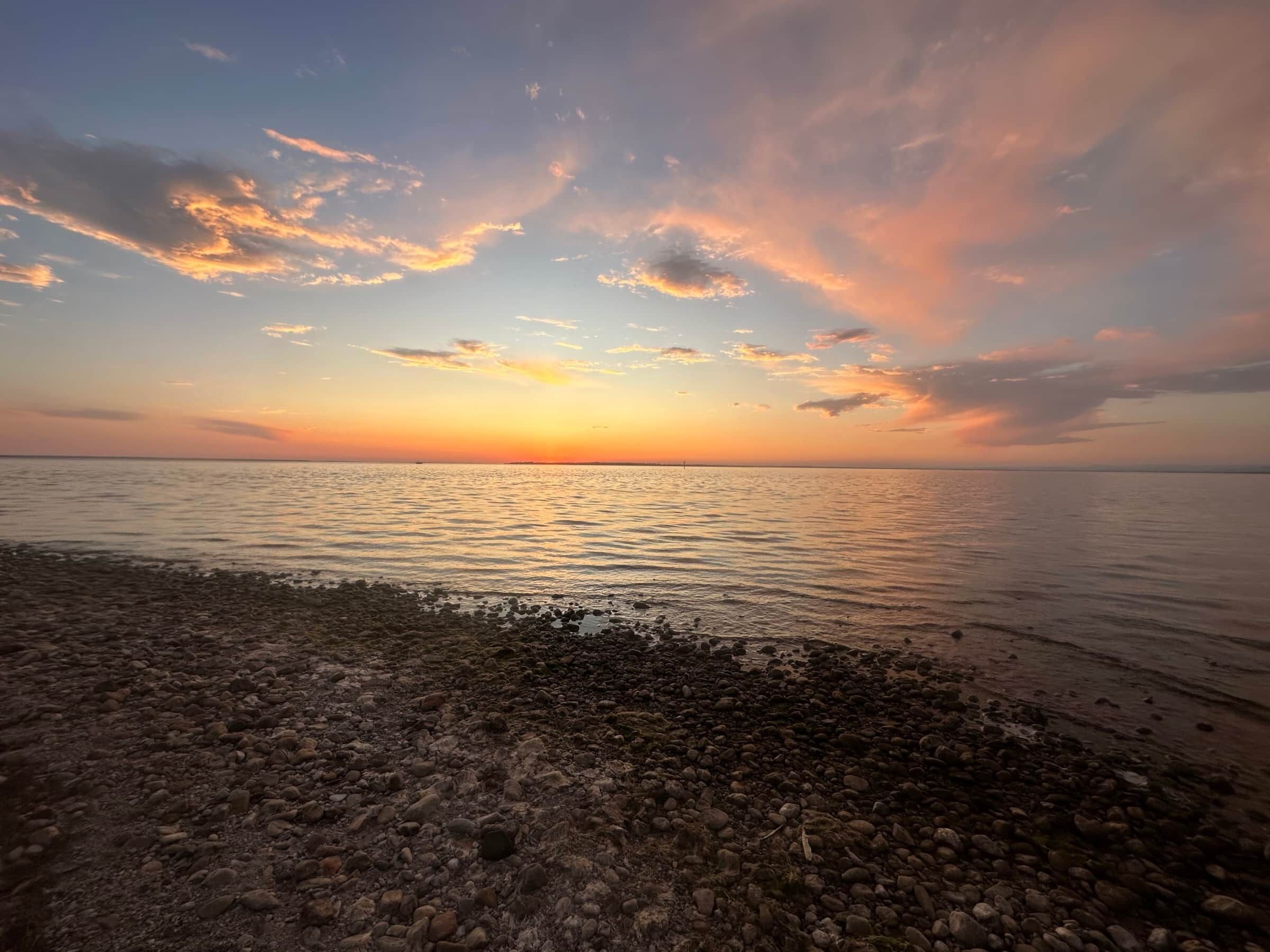 Een strand met een rotsachtige kustlijn en een zonsondergang boven het water.