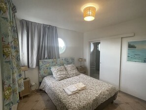 Un dormitori amb llit, cortines, làmpada, taulella de nit, finestra i porta.