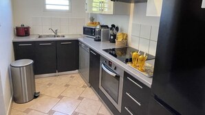Une cuisine moderne avec des meubles de couleur noire, des appareils en acier inoxydable, une fenêtre et une poubelle.