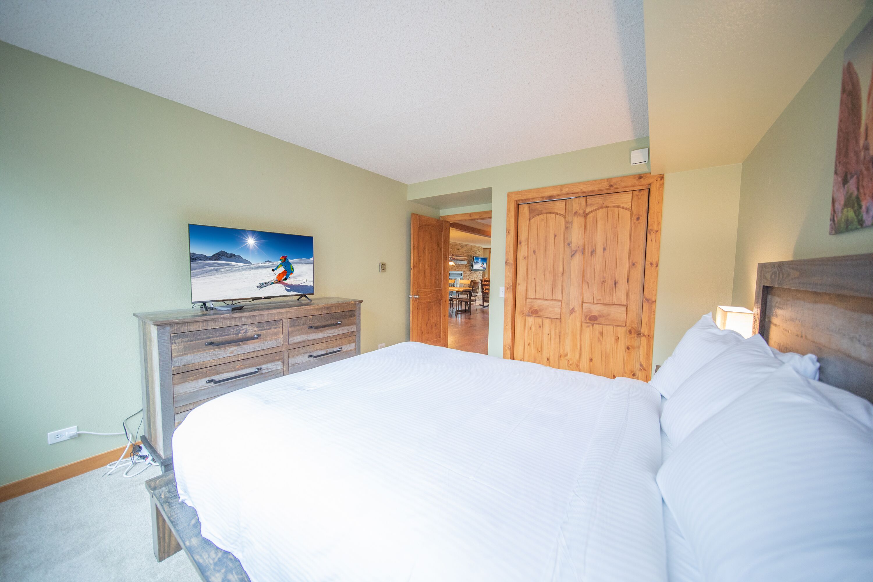 A bedroom with a large bed, wooden dresser, and a television displaying a snowy landscape.