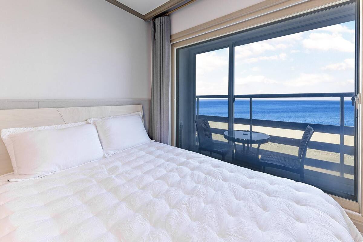 Habitación de hotel con cama, vista al océano y balcón con sillas y una mesa.