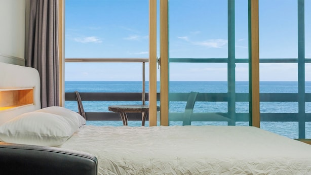 A hotel room with a large window offering a view of the sea, a bed, a chair, and a nightstand. - Sokcho Bird Island Pension (Sokcho)