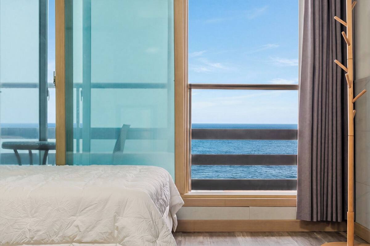 Un dormitorio con un ventanal grande, una cama, una silla y un perchero.