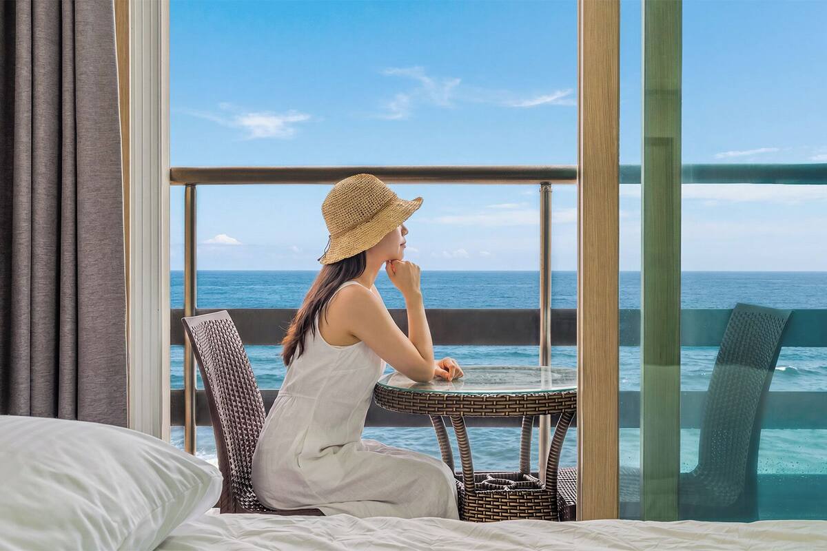 Una habitación con un ventanal grande, una cama, una silla de mimbre y vistas al océano.