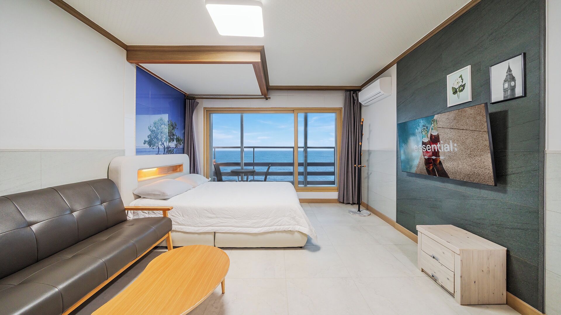 Une chambre d’hôtel avec un lit, un canapé, une télévision et vue sur la mer.
